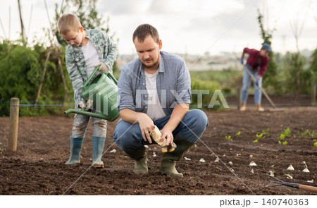 Man planting seeds boy watering beds 140740363