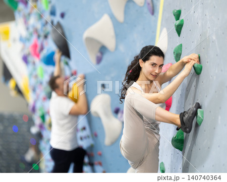 Motivated young girl climbing without ropes and harnesses on artificial bouldering wall in fitness center 140740364