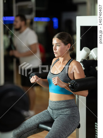 Girl in gym performs exercises for arm muscles using simulators and fitness center equipment. Girl in gym performs exercises for arm muscles using simulators and fitness center equipment. 140740407