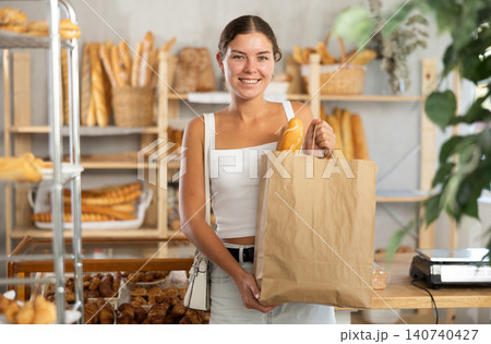 Positive young girl holding baguettes in paper bag in bakery Positive young girl holding baguettes in paper bag in bakery 140740427