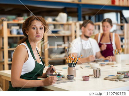 Woman learns to make designs on clay plate using brush and paint in pottery workshop Woman learns to make designs on clay plate using brush and paint in pottery workshop 140740576