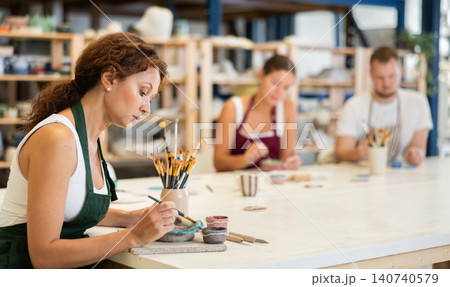 Woman learns to make designs on clay plate using brush and paint in pottery workshop Woman learns to make designs on clay plate using brush and paint in pottery workshop 140740579