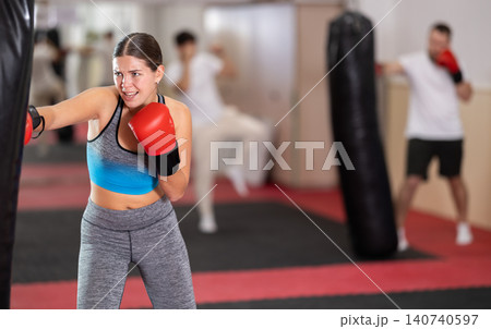 Girl punches and kicks punching bag in gym. Girl punches and kicks punching bag in gym. 140740597