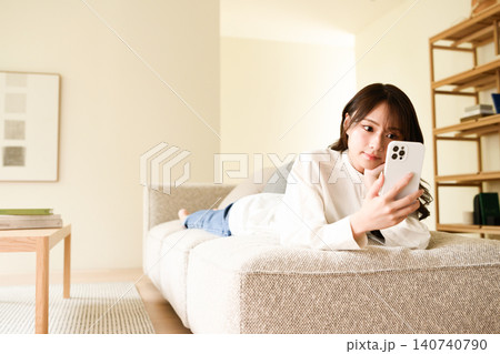 ソファでリラックスしながらスマートフォンを操作する若い女性 ソファでリラックスしながらスマートフォンを操作する若い女性 140740790