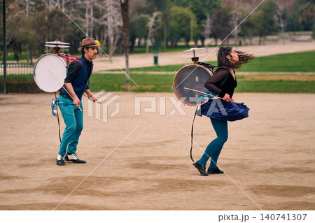 A pair of urban dancers, spinning, playing and dancing, with a bass drum on their backs outdoors, Chilean chinchineros, street musicians who play the bass drum and dance in the streets. A pair of urban dancers, spinning, playing and dancing, with a bass drum on their backs outdoors, Chilean chinchineros, street musicians who play the bass drum and dance in the streets. 140741307