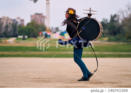 Beautiful Latina woman with a hat dancing with a drum and cymbals on her back, overflowing with joy. Chinchinera, a street musician who dances and plays her drum in the streets. Chilean heritage, Beautiful Latina woman with a hat dancing with a drum and cymbals on her back, overflowing with joy. Chinchinera, a street musician who dances and plays her drum in the streets. Chilean heritage, 140741309