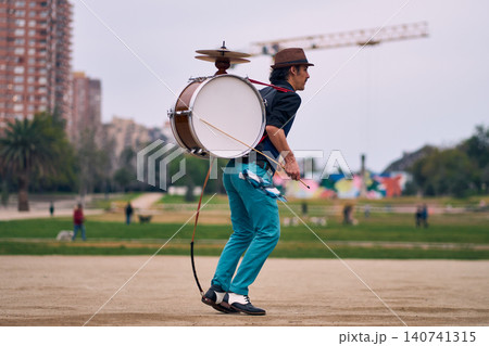 View of a bass drum with a cymbal, a man playing and spinning it, a Chilean chinchinero, a street musician playing the bass drum and dancing in the streets, a Chilean cultural tradition. 140741315