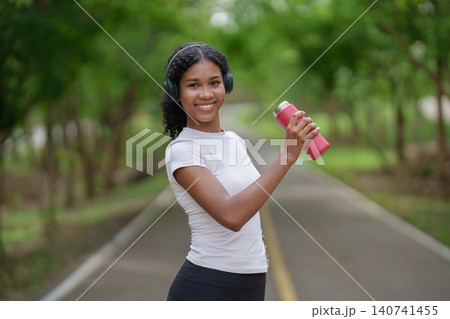 Black woman with water bottle and headphones for outdoor fitness 140741455