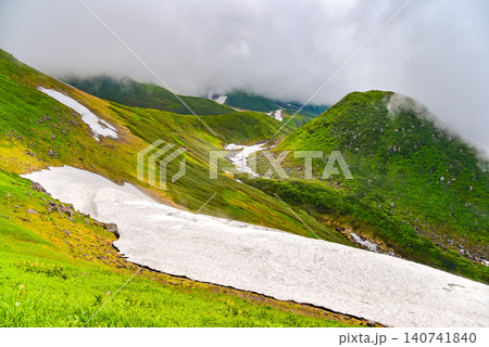 夏の晴れ間 湧き上がる雲に覆われる鳥海山の残雪残る山肌と斜面に流れる雪原風景 夏の晴れ間 湧き上がる雲に覆われる鳥海山の残雪残る山肌と斜面に流れる雪原風景 140741840