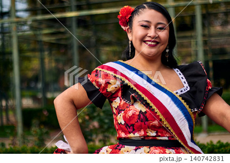 Portrait of a beautiful young woman smiling, cheerfully dressed as a Chilean huasa, joyfully celebrating and posing to dance the cueca, a traditional Chilean dance. Chilean traditions. Portrait of a beautiful young woman smiling, cheerfully dressed as a Chilean huasa, joyfully celebrating and posing to dance the cueca, a traditional Chilean dance. Chilean traditions. 140742831