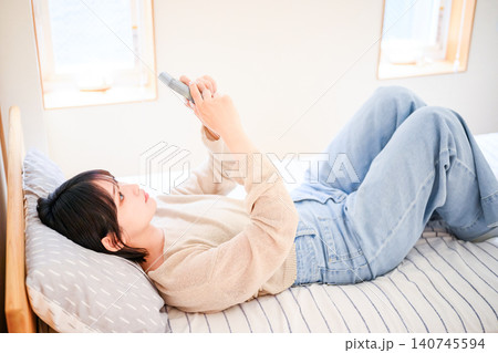 ベッドでくつろぎながらゲームを楽しむ20代日本人女性 ベッドでくつろぎながらゲームを楽しむ20代日本人女性 140745594