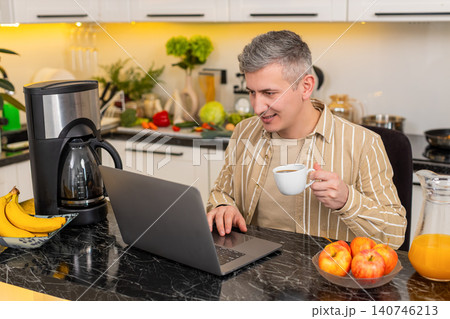 Middle-aged man working on laptop with coffee in kitchen for freelance work and remote business task Middle-aged man working on laptop with coffee in kitchen for freelance work and remote business task 140746213