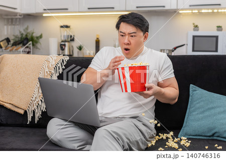 Asian man watches suspense film jumps at jump scare drops popcorn breathes slow then resumes watch Asian man watches suspense film jumps at jump scare drops popcorn breathes slow then resumes watch 140746316