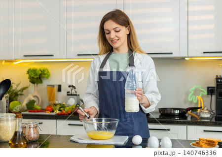 Middle-aged woman whisking eggs with milk in home kitchen for healthy breakfast meal prep nutrition Middle-aged woman whisking eggs with milk in home kitchen for healthy breakfast meal prep nutrition 140746336