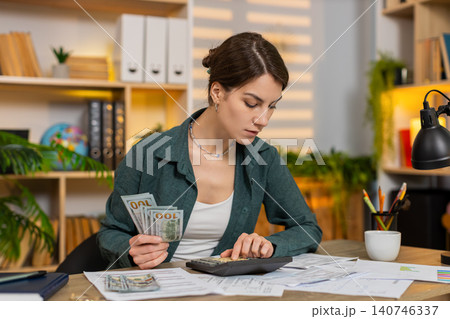 Young woman on home table calculating budget with cash bills receipts and documents at desk indoors 140746337