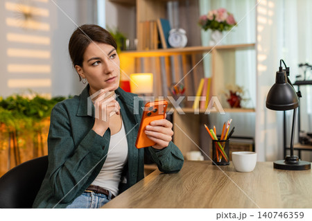 Young woman on home table scrolling smartphone feeling bored tired during remote work break indoors 140746359