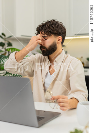 Indian man tired remote worker with laptop in glasses rubbing eyes fighting fatigue continues typing Indian man tired remote worker with laptop in glasses rubbing eyes fighting fatigue continues typing 140746363