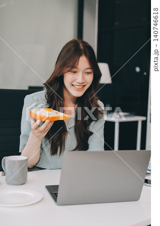 Asian woman reading book eating snack in office Asian woman reading book eating snack in office 140746618