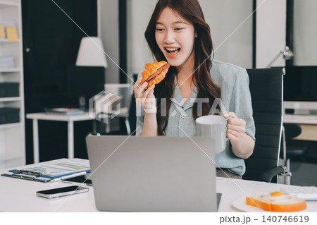 Asian woman reading book eating snack in office Asian woman reading book eating snack in office 140746619