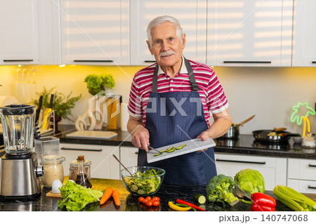 Senior old man mixing cucumber salad in home kitchen for diet plan and healthy nutrition lifestyle Senior old man mixing cucumber salad in home kitchen for diet plan and healthy nutrition lifestyle 140747068