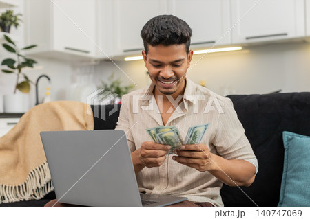 Indian man checks dollar cash with laptop spreadsheet enters sums confirm goal smiles bonus invest Indian man checks dollar cash with laptop spreadsheet enters sums confirm goal smiles bonus invest 140747069