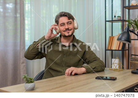 Middle-aged man enjoys music with smartphone headphones nodding head rhythm relaxed content at table 140747078