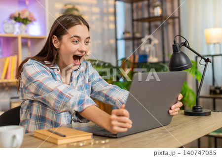 Young woman on home table smiling at laptop celebrating success with applause indoors in living room 140747085