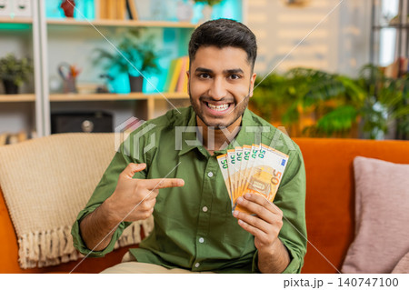 Indian man on home sofa holding cash smiling with joy after win success victory and good profit news 140747100