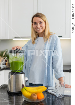 Young woman blending fresh smoothie with apple banana spinach spirulina in home kitchen for morning Young woman blending fresh smoothie with apple banana spinach spirulina in home kitchen for morning 140747354