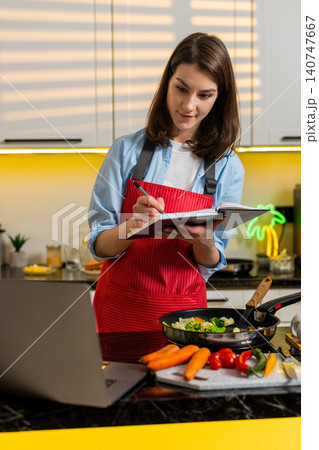 Young woman taking notes from laptop during cooking class for healthy diet meal planning indoor home Young woman taking notes from laptop during cooking class for healthy diet meal planning indoor home 140747667