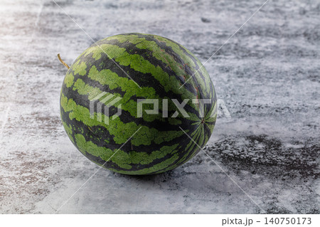 Whole watermelon with green and dark stripes on textured gray surface 140750173
