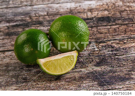 Fresh limes on rustic wooden surface with sliced wedge revealing juicy interior Fresh limes on rustic wooden surface with sliced wedge revealing juicy interior 140750184
