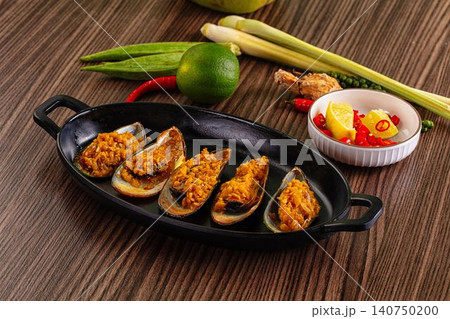 Baked mussels with spicy topping served on black dish with lime lemon chili and lemongrass 140750200