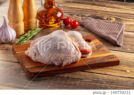 Raw chicken thighs on wooden cutting board with garlic rosemary olive oil and cherry tomatoes Raw chicken thighs on wooden cutting board with garlic rosemary olive oil and cherry tomatoes 140750231