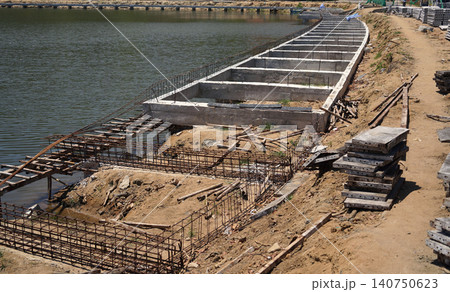 Building process city levee. Exposed foundation rebar grid at site, standing formwork and concrete footings Building process city levee. Exposed foundation rebar grid at site, standing formwork and concrete footings 140750623