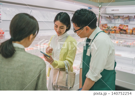 スーパーの精肉売り場でスマホを見せながら笑顔で話す女性客と店員 スーパーの精肉売り場でスマホを見せながら笑顔で話す女性客と店員 140752254