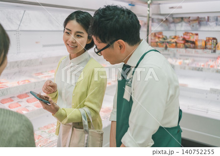 スーパーの精肉売り場でスマートフォンを一緒に見る女性客と店員 スーパーの精肉売り場でスマートフォンを一緒に見る女性客と店員 140752255