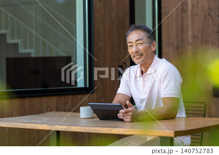 テラスでタブレットを操作しながらコーヒーを飲むシニア男性 140752783
