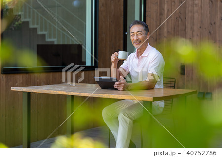 テラスでタブレットを操作しながらコーヒーを飲むシニア男性 140752786