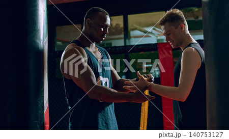 Coach helping boxer wrap hands before workout in dark training gym. 140753127