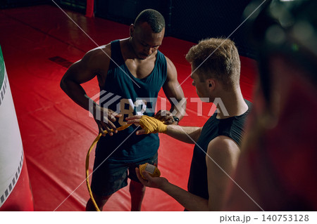 Boxing coach wrapping athlete hands before training session in dark gym. Boxing coach wrapping athlete hands before training session in dark gym. 140753128