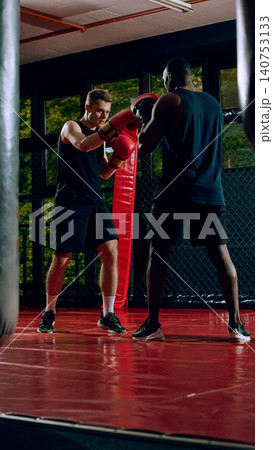 Two male athletes training boxing drills together in dark fight gym Two male athletes training boxing drills together in dark fight gym 140753133