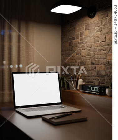 Dim workspace with white screen laptop and digital clock on table beside brick wall under lamp light 140754053