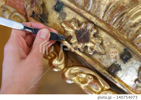 Craftsman Works on Detailed Restoration of a Gilded Wood Sculpture in a Workshop Setting During Daylight Hours Craftsman Works on Detailed Restoration of a Gilded Wood Sculpture in a Workshop Setting During Daylight Hours 140754073
