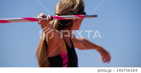 An athlete throwing a javelin in a sporting event. Rear view of female athlete in sportswear throwing javelin An athlete throwing a javelin in a sporting event. Rear view of female athlete in sportswear throwing javelin 140756164