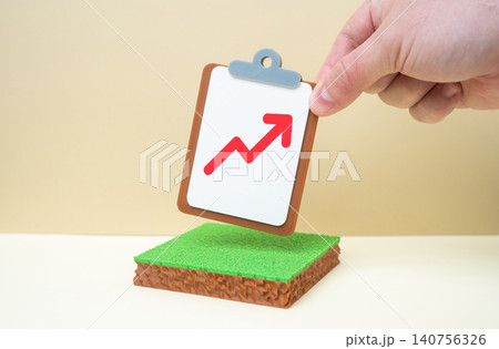 A plot of land and a tablet with a red arrow pointing upward. Rising land prices, increasing rental income. Land tax increases. 140756326