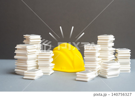 A builder's hard hat amid mountains of paperwork and documents. The bureaucratic construction industry is detrimental to the economy. A builder's hard hat amid mountains of paperwork and documents. The bureaucratic construction industry is detrimental to the economy. 140756327