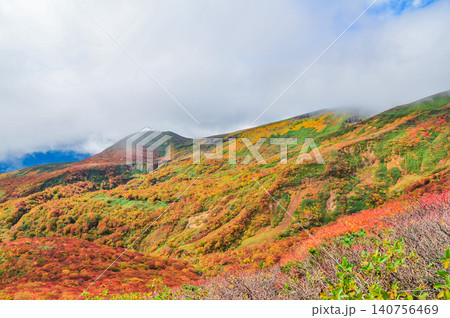 秋の晴れ間 紅葉最盛期の栗駒山・雲間から青空覗く全山紅葉の美しい山肌風景 140756469