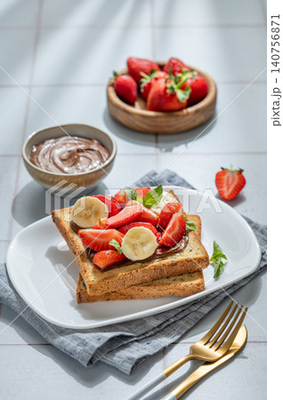 Toasted bread with chocolate cream, strawberries, and banana on a plate on a tile background Toasted bread with chocolate cream, strawberries, and banana on a plate on a tile background 140756871