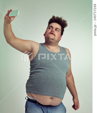 Selfie, fashion and plus size man in studio posing with casual, trendy and cool outfit with stomach. Style, serious and crazy male person with photography picture isolated by gray background. Selfie, fashion and plus size man in studio posing with casual, trendy and cool outfit with stomach. Style, serious and crazy male person with photography picture isolated by gray background. 140757289